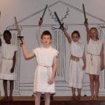 Students in white robe costumes hold their swords up to the sky in their school play