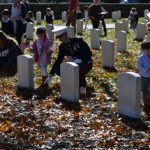 Joseph Bush teaches students about Veterans Day by placing American flags in front of tombstones