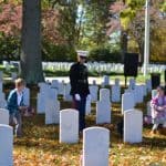 Veteran and family pay respects to other veteran tombstones by placing American flags in front of them