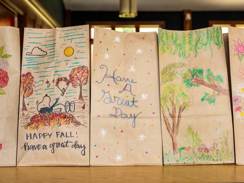 Paper bags with different colorful autumn drawings on them sit in a row on a table in Highlands Latin School