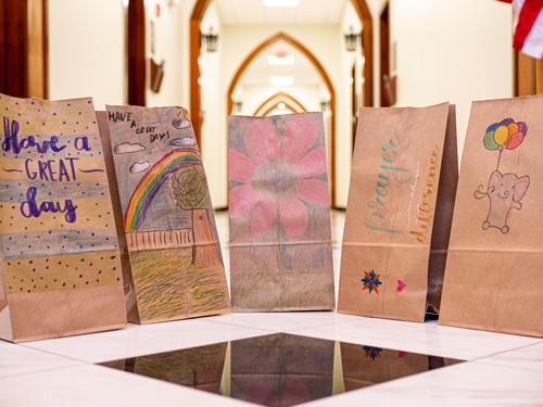 5 brown paper bags with colored drawings on them sit in the hallway of the Highlands Latin School upper school building