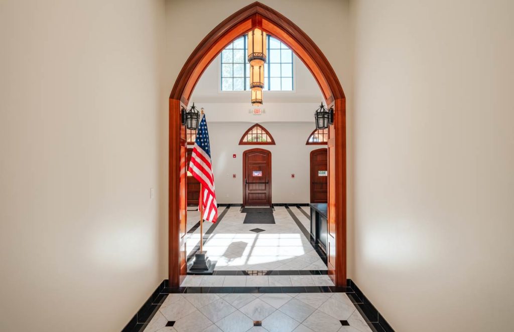 An American flag sits in the main entrance of Highlands Latin Upper School lobby with granite tile floors and an arched hallway ceiling