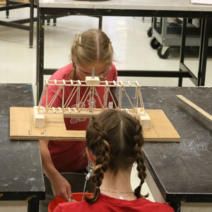 Two Highlands Latin School students test the durability of a homemade popsicle bridge between two desks